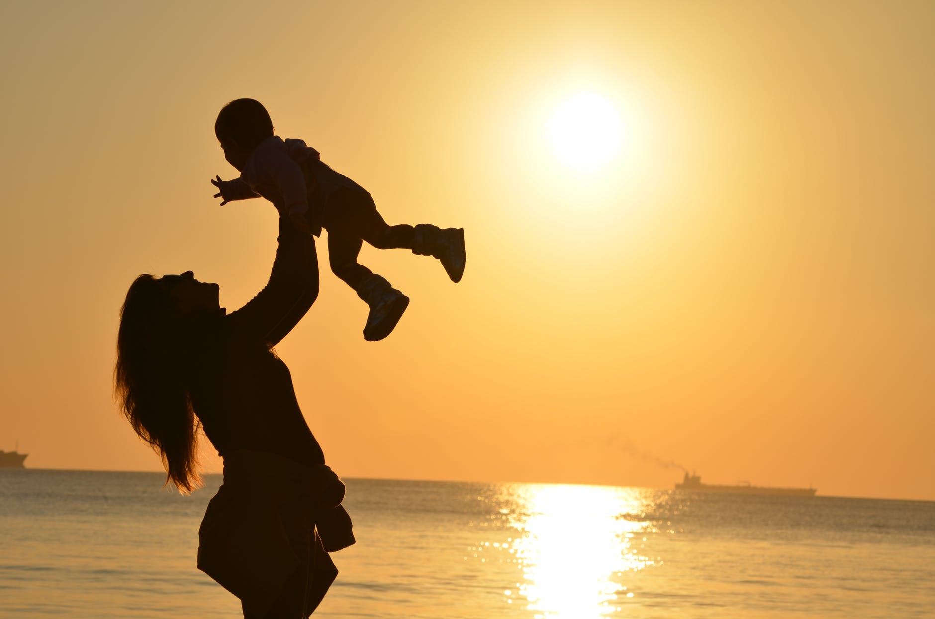 Foto de silueta de una madre con su bebé en la playa durante la hora dorada